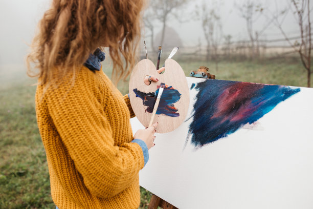 近距离的照片年轻的女艺术家工作在绘画户外。她拿着油画颜料，艺术家的画笔，帆布和调色板。她在调色板上调色。手关闭。图片下载