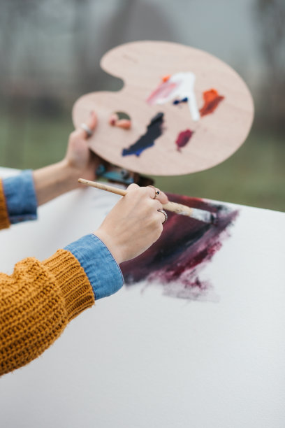 近距离的照片年轻的女艺术家工作在绘画户外。她拿着油画颜料，艺术家的画笔，帆布和调色板。她在调色板上调色。手关闭。图片下载