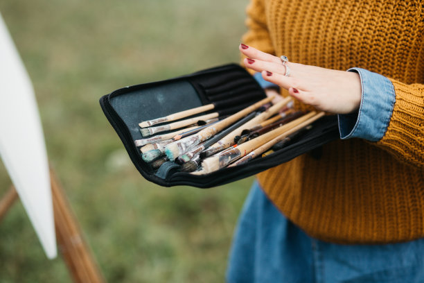 近距离的照片年轻的女艺术家工作在绘画户外。她拿着油画颜料，艺术家的画笔，帆布和调色板。她在调色板上调色。手关闭。图片下载