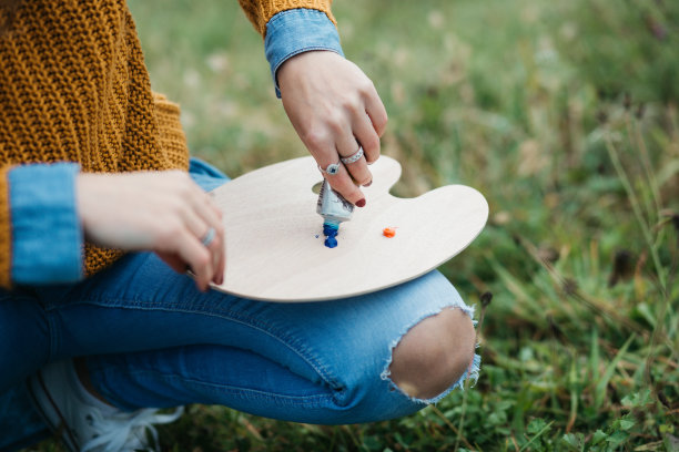 近距离的照片年轻的女艺术家工作在绘画户外。她拿着油画颜料，艺术家的画笔，帆布和调色板。她在调色板上调色。手关闭。图片下载