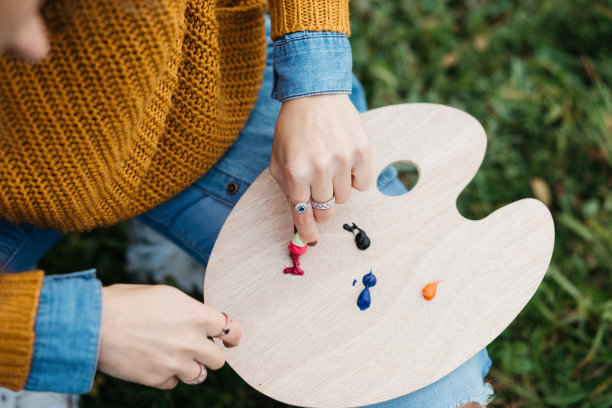 近距离的照片年轻的女艺术家工作在绘画户外。她拿着油画颜料，艺术家的画笔，帆布和调色板。她在调色板上调色。手关闭。图片下载