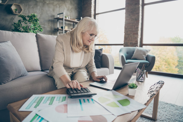 惊人的白发老奶奶使用笔记本阅读电子邮件同事报告启动计数计算器税坐在沙发沙发房间办公室室内的资料照片图片下载