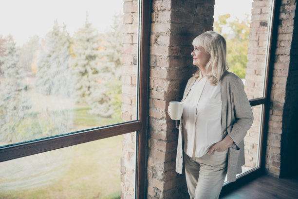 照片惊人的金发可爱的年老的奶奶家好心情喝热饮看起来梦幻的窗户站在砖墙附近的室内图片下载