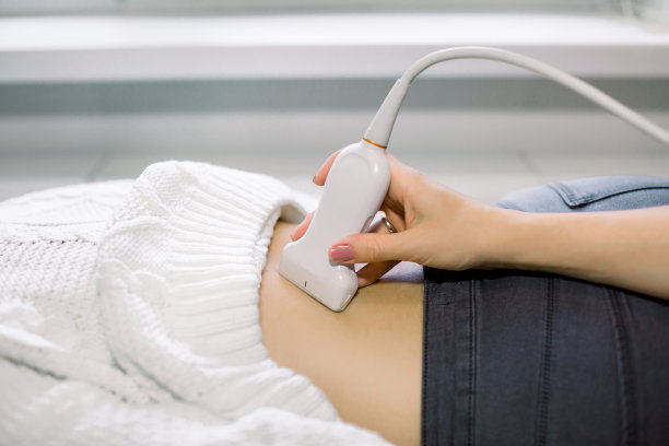 近距离照片下背部的年轻女子得到超声测试在诊所。拿着超声波扫描仪的医生的手图片下载