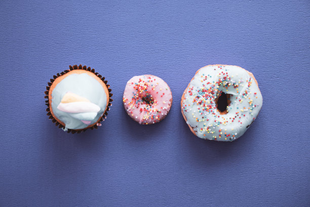 彩色背景的甜甜圈，两个甜甜圈和一个纸杯蛋糕，上面有糖果。顶视图的照片图片下载
