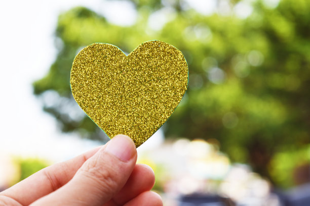 手握黄金心脏形状在软焦点背景。情人节快乐创意概念。图片下载