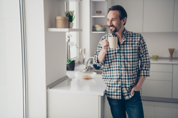 英俊的积极乐观的好高兴有吸引力的家伙拿着一杯新鲜的可可豆在手里看着窗外的落叶站在厨房的照片图片下载