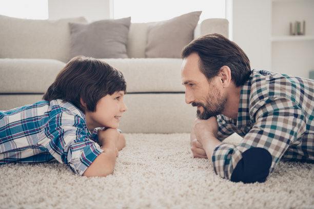 近距离的照片肖像英俊的胡子在格子衬衫的家伙和他的愉快的积极乐观的儿子躺在舒适的毛茸茸的地毯附近的沙发看着眼睛在客厅图片下载