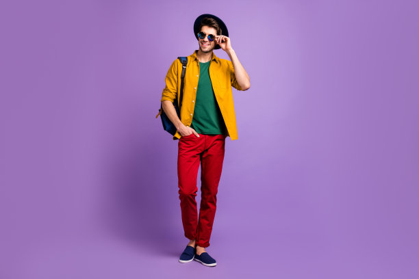 积极开朗的现代男孩的全长照片休息，放松，走路，保持背包，调整他的眼镜，穿蓝色复古的头饰，时尚的衣服孤立在紫罗兰色的背景图片下载