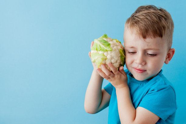 小男孩手捧花椰菜以蓝色为背景，以饮食和锻炼为良好的健康理念图片下载