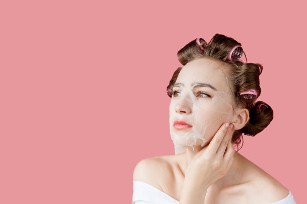 漂亮的年轻女孩戴着面具，卷发器碰着脸。图片下载