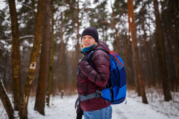 照片的侧视图微笑的女孩在帽子和背包在冬天的森林图片下载