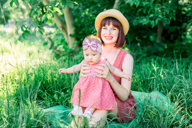 一个快乐的家庭在一个阳光明媚的春天在绿色的花园野餐:一个美丽的微笑的母亲坐在绿色的草地上，她的小女儿笑着坐在她的腿上图片下载