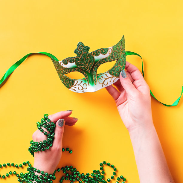 狂欢节饰品平铺在亮黄色的背景上，俯视图，复制空间。女人拿着狂欢节的面具和珠子。节日节日概念开销图片下载