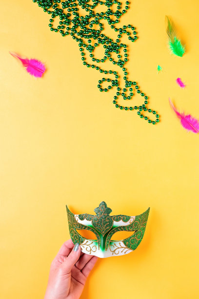 狂欢节饰品平铺在亮黄色的背景上，俯视图，复制空间。女人拿着狂欢节的面具和珠子。节日节日概念开销图片下载