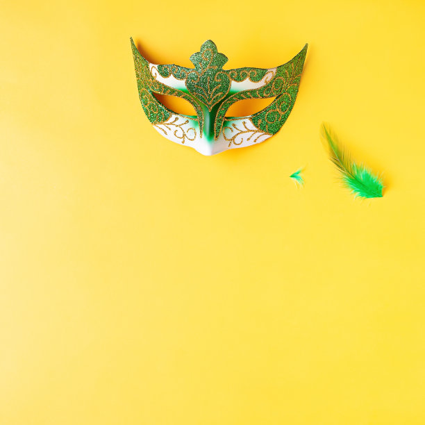 狂欢节饰品平铺在亮黄色的背景上，俯视图，复制空间。框架上有传统的狂欢节珠子，面具，扁平的羽毛。嘉年华假日概念图片下载