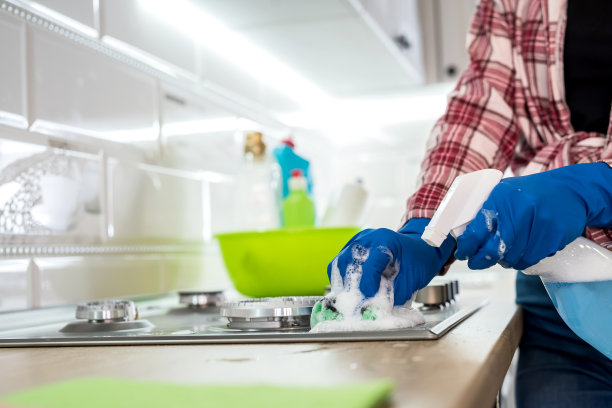 用海绵和橡胶保护手套擦拭烤箱顶部的女人。图片下载