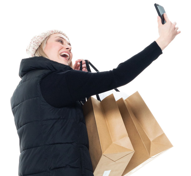 年轻女性摄影蹲下戴着针织帽，拿着包和使用智能手机图片下载