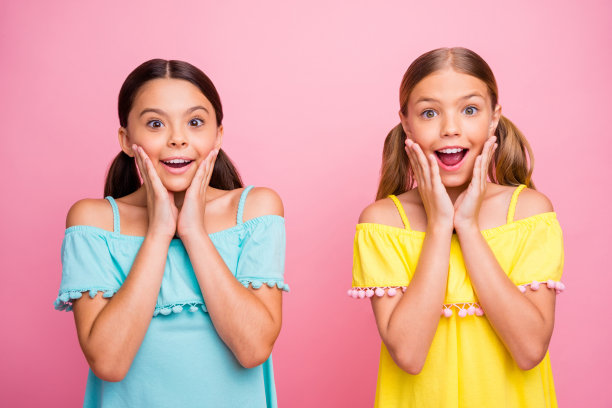 照片的两个美丽的小学校女模特同学庆祝暑假开始穿亮蓝色的黄色衬衫连衣裙孤立的粉红色背景图片下载