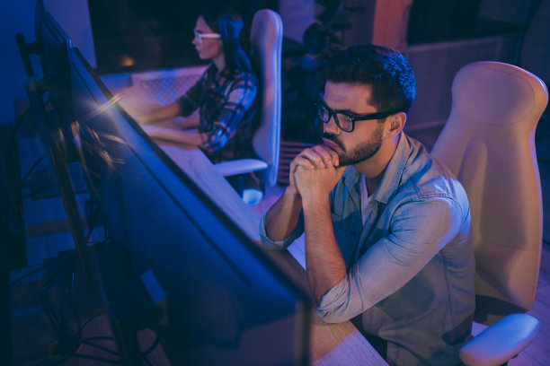 it专家的照片，两个男人女士商务人员坐在深夜椅子一起看监视器检查错误修改系统编写界面前端代码办公室室内图片下载