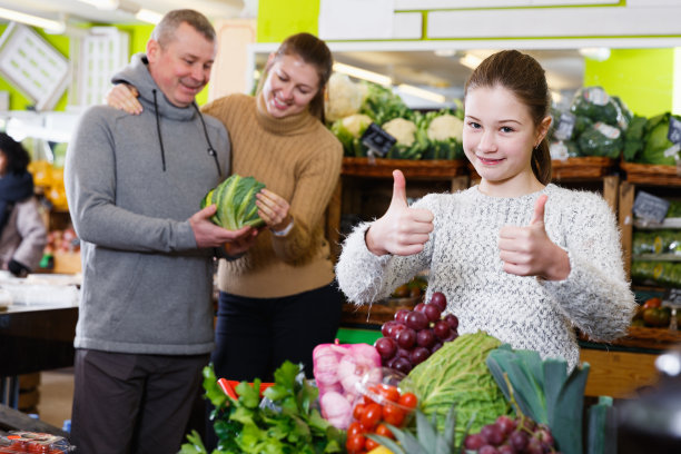 微笑的女孩和父母在蔬菜店购物图片下载