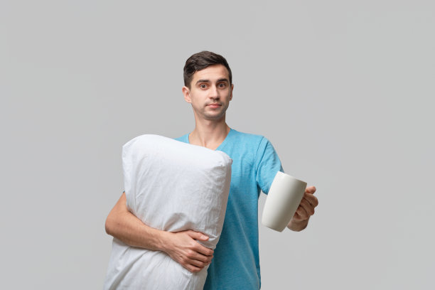 年轻的黑发男子拿着白色的咖啡和白色的枕头图片下载