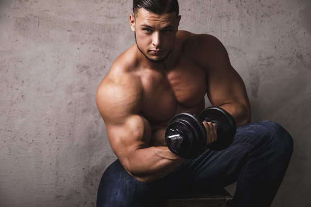 一个巨大的健美运动员在用哑铃做二头肌卷曲运动图片下载