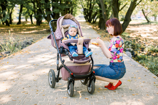 妈妈在公园里用勺子喂推着婴儿车的孩子素材图片