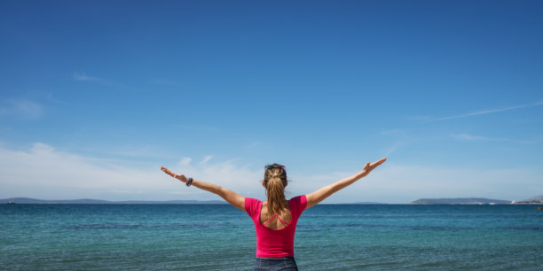 一个年轻女子站在海边，张开双臂庆祝生命图片下载
