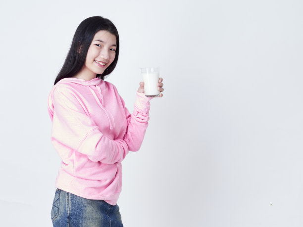 可爱的女孩拿着一杯牛奶，而站在白色的背景。图片下载