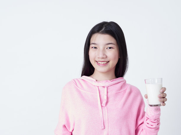 可爱的女孩拿着一杯牛奶，而站在白色的背景。图片下载