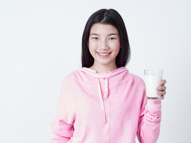 可爱的女孩拿着一杯牛奶，而站在白色的背景。图片下载