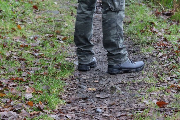 一张照片，一个男人的脚站在森林的小路上。迷彩裤和登山靴。潮湿天气，徒步旅行，户外概念。图片下载