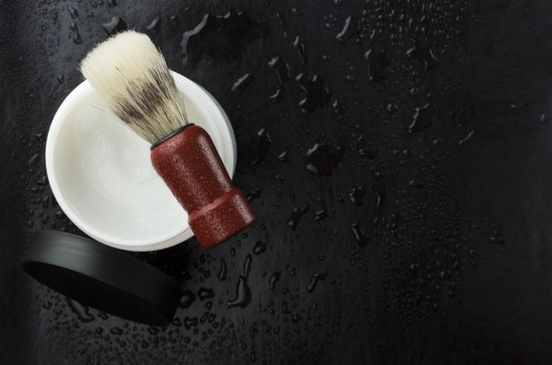 剃须泡沫罐俯视图，木柄刷，黑色表面有水滴。文本空白图片下载