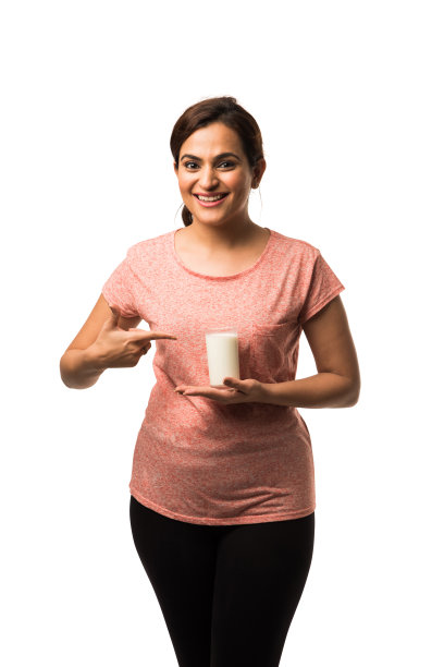 肖像年轻的印度/亚洲妇女喝牛奶从玻璃隔离在白色的背景图片下载