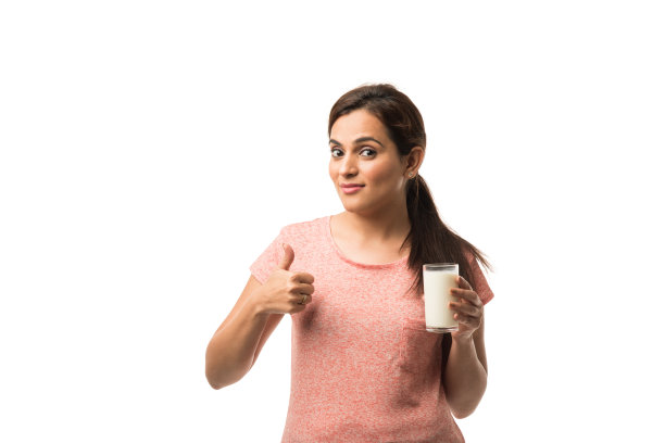 肖像年轻的印度/亚洲妇女喝牛奶从玻璃隔离在白色的背景图片下载