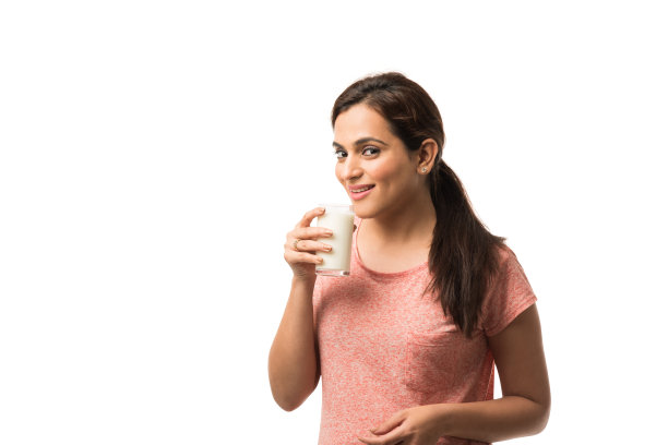 肖像年轻的印度/亚洲妇女喝牛奶从玻璃隔离在白色的背景图片下载