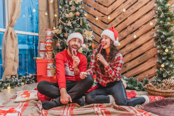 全身照片的年轻人在红色的衣服和圣诞老人的帽子，品尝美味的糖果在圣诞气氛。图片下载