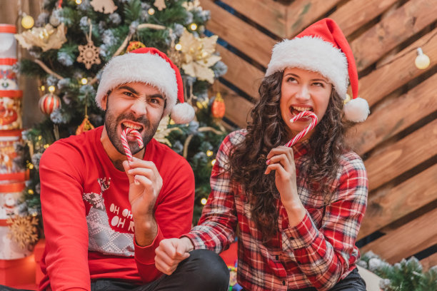 年轻人穿着红衣服，戴着圣诞帽，在圣诞气氛中品尝美味的糖果，但是糖果太硬了，咬不动。图片下载