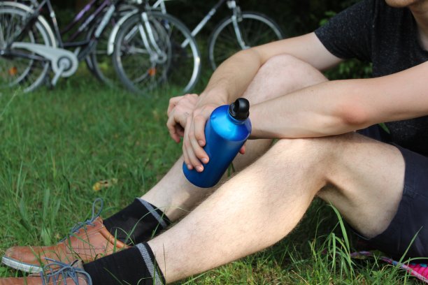 男性骑自行车的人正坐在草地上休息，手里拿着一个金属瓶子图片下载