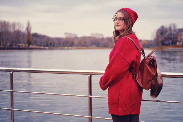 一位穿着红毛衣的年轻女子站在湖的背景上图片下载