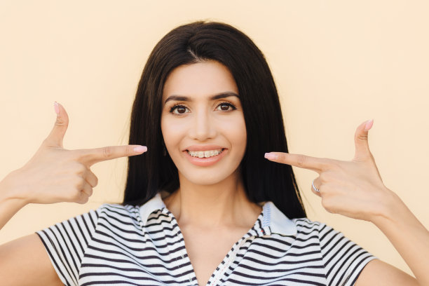 人、美与广告理念。深色头发的年轻女子带着温柔的微笑，嘴角露出灿烂的笑容，有背带，穿着休闲条纹t恤，孤立在光线工作室的背景下图片下载