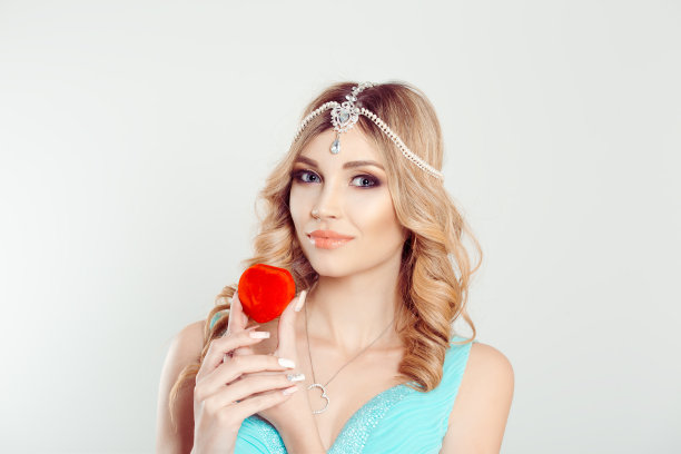 我恋爱了。金发碧眼的女子在东方珠宝头上戴着心形的订婚戒指礼盒看着你的相机孤立的白色灰色背景墙图片下载