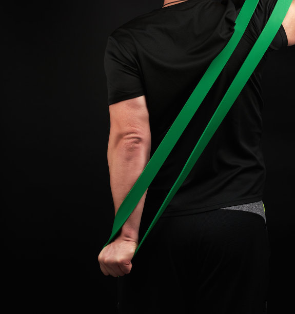 身着黑色制服的成年运动员站在身后，拉开绿色的运动松紧带图片下载
