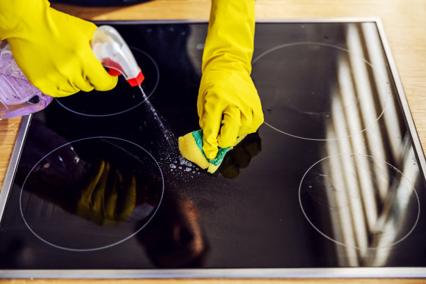 俯视图的值得男人喷洒清洁产品在炉子上，并与海绵摩擦。手上戴着橡胶手套。图片下载