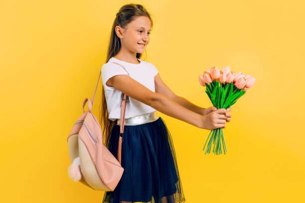 美丽的女学生去学校与一束花在一个黄色的背景图片下载