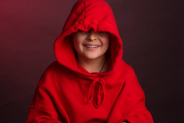 一个黑头发的男孩的工作室肖像，在栗色的背景，在一个红色帽衫夹克图片下载