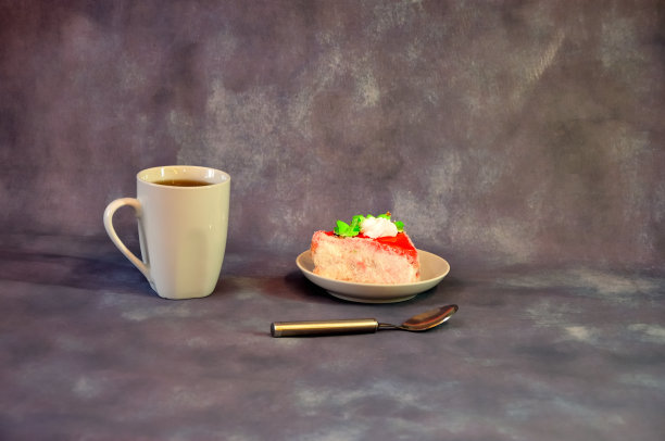 一个高大的白瓷咖啡杯和一个盘子，上面有一个三角形的饼干蛋糕，上面有白色奶油和红色糖霜。图片下载
