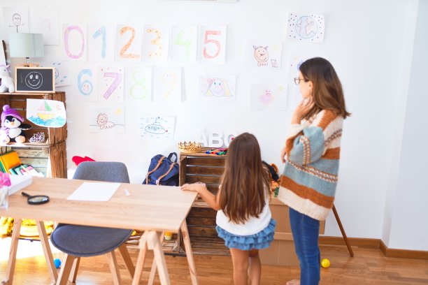 美丽的老师和蹒跚学步的孩子看着墙上的画在许多玩具在幼儿园图片下载