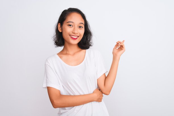 年轻的中国女子穿着休闲t恤站在孤立的白色背景上，脸上带着大大的微笑，用手和手指指着一边看着镜头。图片下载